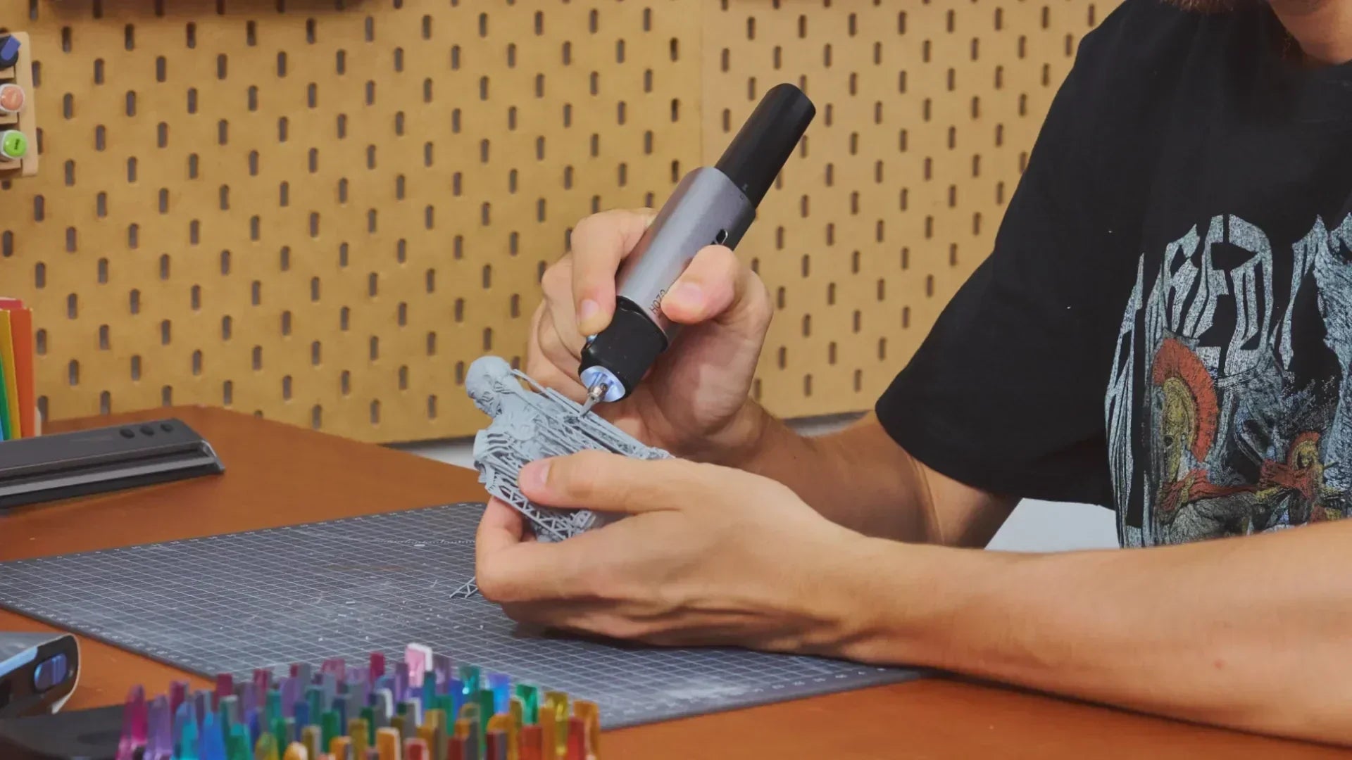Person using a rotary tool on a workbench with a pegboard background.