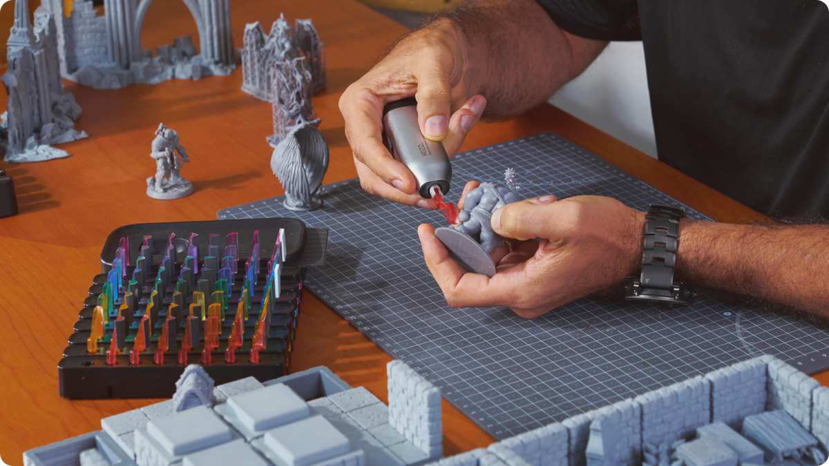 Hands holding a small gray figure while a silver rotary tool touches it.