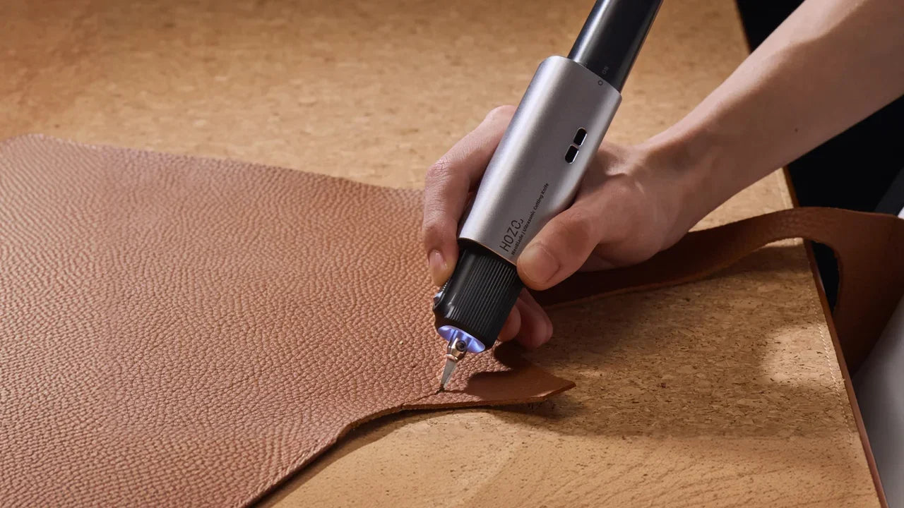 Hand‑held HOZO ultrasonic cutting knife precisely cutting brown grain leather for handmade leatherwork