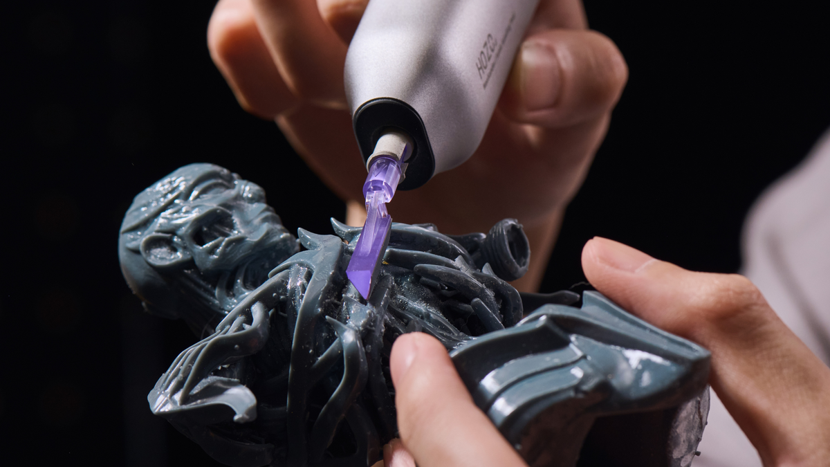 A hobbyist using the HOZO electric precision sander to carefully polish intricate textured details on a miniature monster resin figurine.